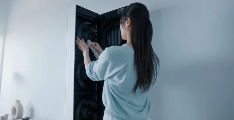 해당 이미지는 하늘색 배경에 LG 휘센 AI 오브제컬렉션 뷰I 스탠드 에어컨이 열려 있으며, 하늘색 상의를 입은 여성이 하얀색 천을 들고 팬을 닦고 있는 모습입니다. 