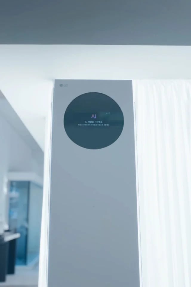 AI바람 기능을 설명하는 썸네일 이미지로 밝은 실내 공간 중앙에 스탠드형 에어컨이 설치되어 있으며, 상단의 원형 블랙 디지털 디스플레이가 보입니다. 에어컨의 한쪽 토출구에서 푸른색 선 형태의 기류 그래픽이 실내 전반으로 퍼져 있습니다. LG WHISEN AI AI바람 이라는 문구가 표시되어 있습니다. 오른쪽에는 커튼과 벽면 구조가 보이는 주거 공간이 이어집니다. 이 이미지는 AI 제어를 통해 실내로 바람을 고르게 분산시키는 에어컨의 바람 제어 기능을 설명합니다.