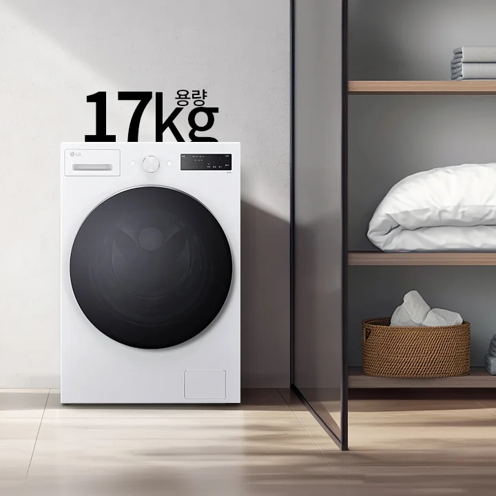 세탁기 이미지로, 중앙에 흰색 드럼세탁기가 놓여 있으며, 세탁기 위에는 17kg 용량이라는 텍스트가 있습니다. 세탁기 왼쪽에는 금색 수도꼭지가 있는 흰색 욕조가 보이며, 오른쪽에는 수건과 이불이 정리된 선반이 있습니다.